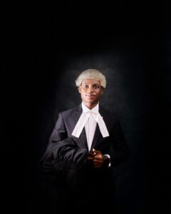 Portrait of a young lawyer holding a gown, wearing a wig, and showing confidence.